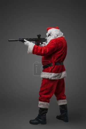 Photo for Shot of christmas santa claus with red costume and rifle against gray background. - Royalty Free Image