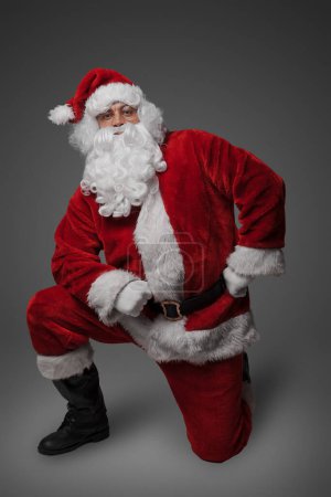 Téléchargez les photos : Prise de vue de Père Noël claus avec chapeau d'hiver et vêtements regardant la caméra tout en étant assis. - en image libre de droit