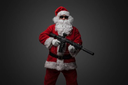Photo for Shot of santa claus gunslinger with rifle and sunglasses dressed in red costume. - Royalty Free Image
