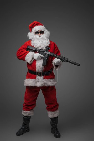 Foto de Tiro de pistolero de Santa Claus con rifle y gafas de sol vestidas con traje rojo. - Imagen libre de derechos
