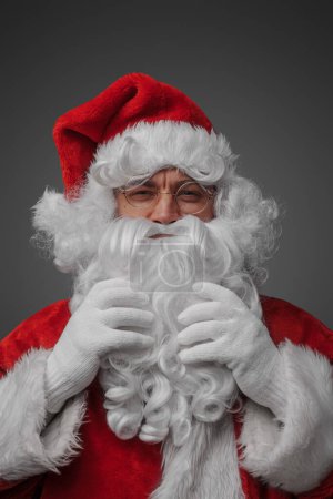 Photo for Portrait of christmas santa claus with glasses stroking his beard looking at camera. - Royalty Free Image