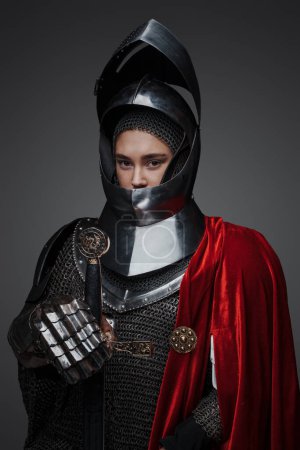 Photo for Portrait of knight woman with sword and red cloak isolated on grey background. - Royalty Free Image