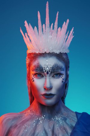 Téléchargez les photos : Portrait de charmante reine des neiges sous éclairage rouge sur fond bleu. - en image libre de droit