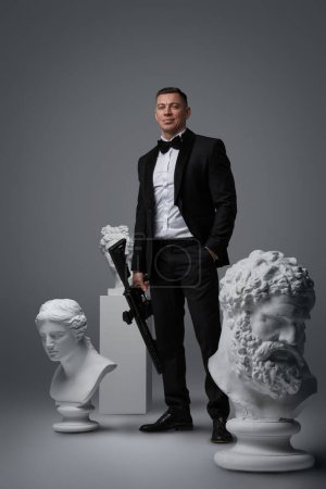 Photo for Studio shot of secret agent with rifle dressed in suit around greek sculptures. - Royalty Free Image