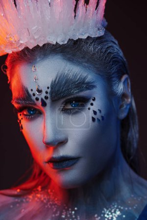 Téléchargez les photos : Portrait de charmante reine des neiges sous éclairage rouge sur fond bleu. - en image libre de droit