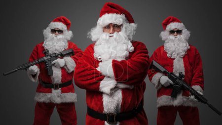 Photo for Studio shot of santa posing with crossed arms and two santa with rifles standing on his sides. - Royalty Free Image