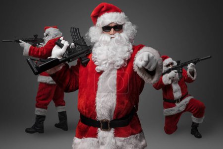 Téléchargez les photos : Portrait de Père Noël branché avec costume rouge et fusil pointant vers la caméra. - en image libre de droit