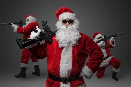 Photo for Studio shot of stylish crew of three Santa with rifles isolated on grey background. - Royalty Free Image
