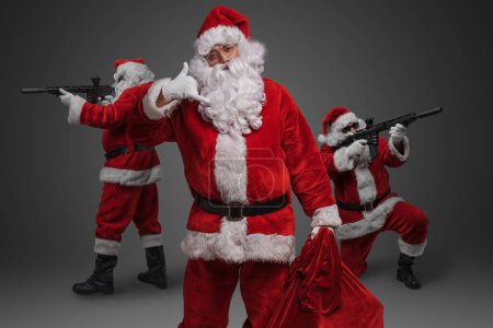 Téléchargez les photos : Portrait de trois Père Noël habillé en costume rouge un avec sac et deux avec fusils. - en image libre de droit