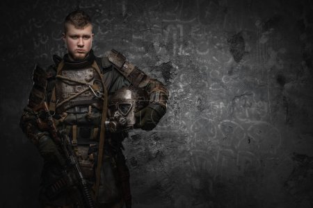 Foto de Portrait of military man dressed in ragged armor holding helmet and shotgun. - Imagen libre de derechos