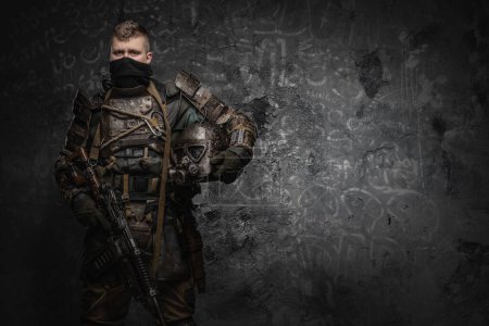 Téléchargez les photos : Portrait of military man dressed in ragged armor holding helmet and shotgun. - en image libre de droit
