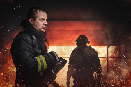 Foto de Shot of brave fireman dressed in uniform putting out fire in burning city. - Imagen libre de derechos