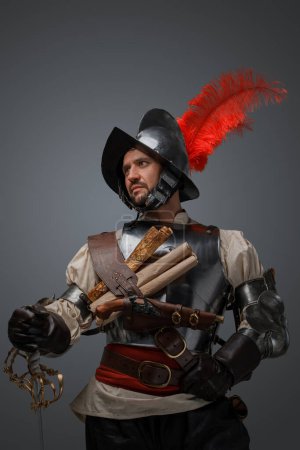 Foto de Shot of musketeer of renaissance period dressed in plate armor holding epee. - Imagen libre de derechos