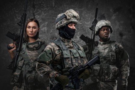 Photo for Multiethnic military team of three soldiers with rifles against grey background. - Royalty Free Image