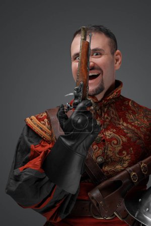 Foto de Retrato de conquistador sonriente con pistola vestida con traje rojo mirando a la cámara. - Imagen libre de derechos