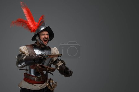 Foto de Portrait of antique furious musketeer dressed in steel plate armor holding pistol. - Imagen libre de derechos