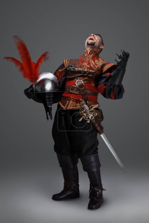 Photo for Shot of angry conquistador knight with epee holding plumed helmet. - Royalty Free Image