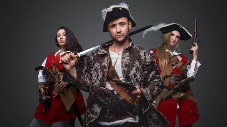Photo for Shot of pirate man and two women with flintlock guns against grey background. - Royalty Free Image