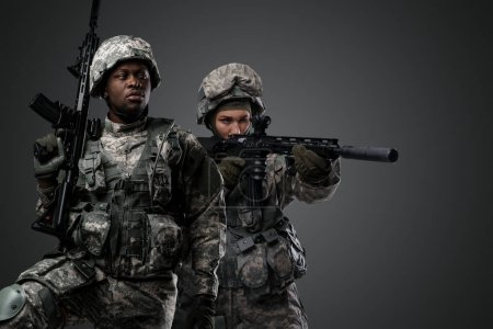 Téléchargez les photos : Studio shot de soldat noir regardant loin et camarade féminin avec fusil. - en image libre de droit