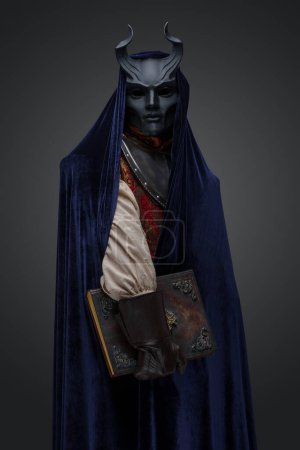 Photo for Shot of cultist with horned mask and dark blue cape against gray background. - Royalty Free Image