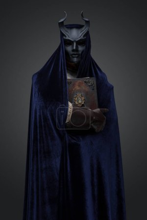 Photo for Shot of dark cultist dressed in horned mask and robe holding book. - Royalty Free Image