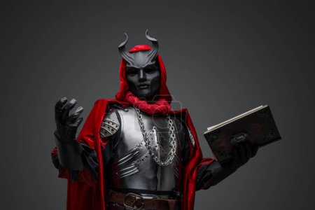 Foto de Portrait of evil knight with book dressed in red robe and plate armor. - Imagen libre de derechos