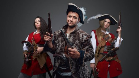 Photo for Shot of pirate man and two women with flintlock guns against grey background. - Royalty Free Image