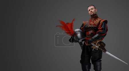 Photo for Portrait of fashionable musketeer swordsman with helmet isolated on gray. - Royalty Free Image