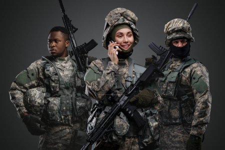 Photo for Shot of soldier woman talking on smartphone near comrades against gray background. - Royalty Free Image
