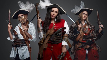 Photo for Shot of isolated on grey three female pirates dressed in costumes holding pistols. - Royalty Free Image