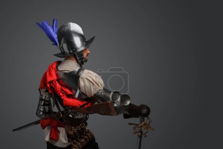 Téléchargez les photos : Portrait of conquistador dressed in plate armor posing with sword looking away. - en image libre de droit