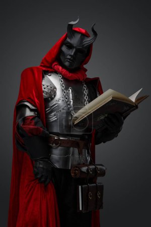 Foto de Retrato de espeluznante caballero oscuro con armadura de placa y libro de celebración de máscara. - Imagen libre de derechos