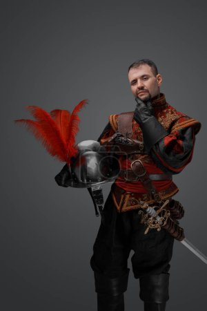 Photo for Portrait of fashionable musketeer swordsman with helmet isolated on gray. - Royalty Free Image