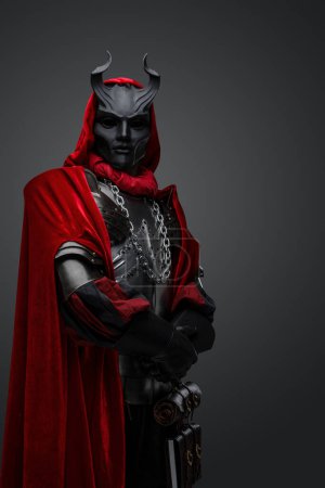 Foto de Retrato de culto medieval con capa roja y máscara negra vestida con armadura de acero. - Imagen libre de derechos
