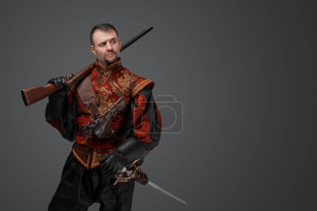 Photo for Shot of medieval musketeer man dressed in antique stylish suit holding rifle. - Royalty Free Image