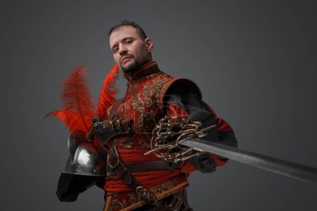 Photo for Shot of medieval musketeer swordsman with epee and helmet against gray background. - Royalty Free Image