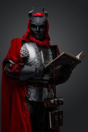 Foto de Retrato de espeluznante caballero oscuro con armadura de placa y libro de celebración de máscara. - Imagen libre de derechos