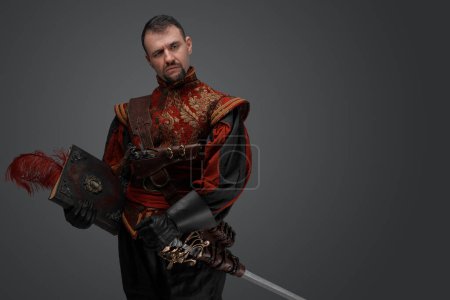 Téléchargez les photos : Portrait of musketeer duelist dressed in stylish suit holding book looking at camera. - en image libre de droit