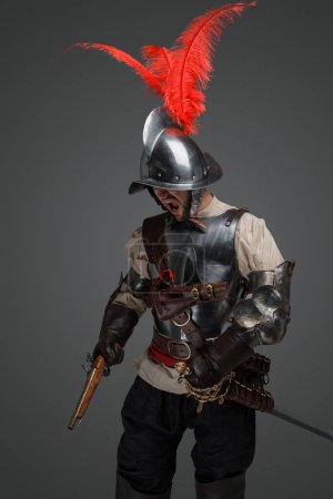 Téléchargez les photos : Studio shot of isolated on grey musketeer with sword and pistol dressed in armor. - en image libre de droit