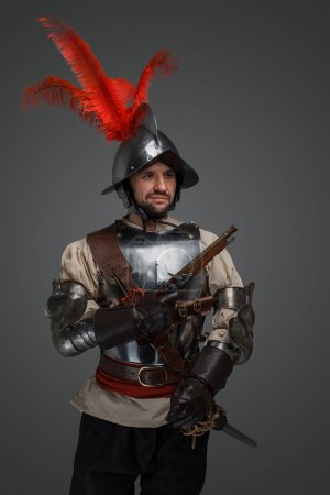 Foto de Studio shot of isolated on grey musketeer with sword and pistol dressed in armor. - Imagen libre de derechos