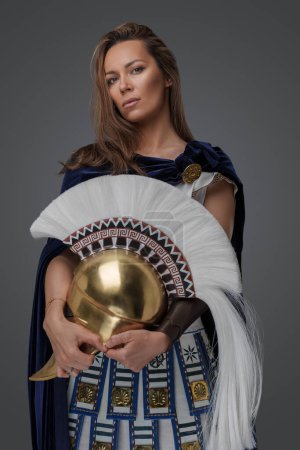 Foto de Estudio de mujer guerrera griega vestida con armadura sosteniendo casco dorado. - Imagen libre de derechos