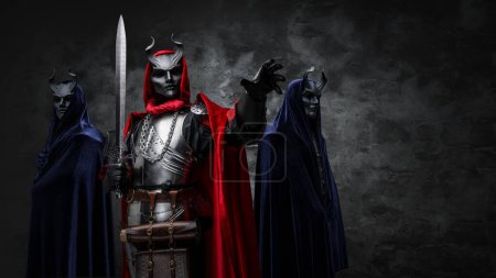 Foto de Retrato de ogranización esotérica de tres personas vestidas con túnicas y máscaras con cuernos. - Imagen libre de derechos