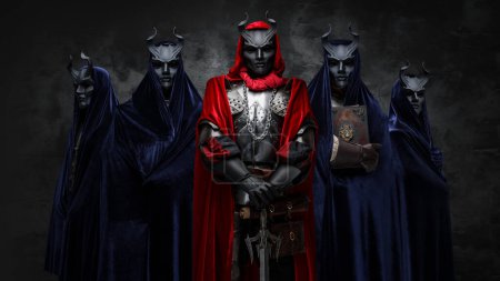 Foto de Disparo de cinco hermanos de culto místico vestidos con mantos oscuros y máscaras con cuernos. - Imagen libre de derechos