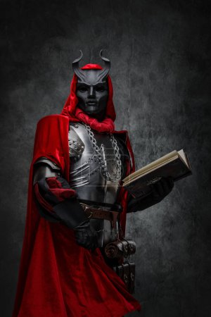 Photo for Shot of mysterious cultist dressed in steel armor and red mantle holding book. - Royalty Free Image