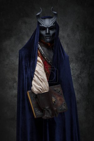 Foto de Retrato de oración de culto esotérico vestido con túnica oscura y máscara con cuernos. - Imagen libre de derechos
