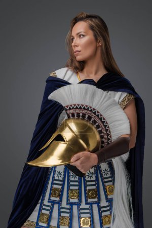 Photo for Studio shot of greek warlord woman dressed in armor holding golden helmet. - Royalty Free Image