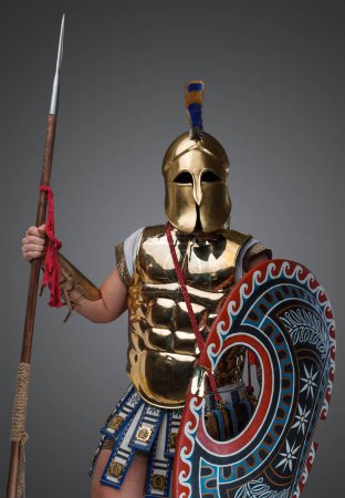 Foto de Retrato de guerrero griego aislado sobre fondo gris vestido con armadura y casco de bronce. - Imagen libre de derechos