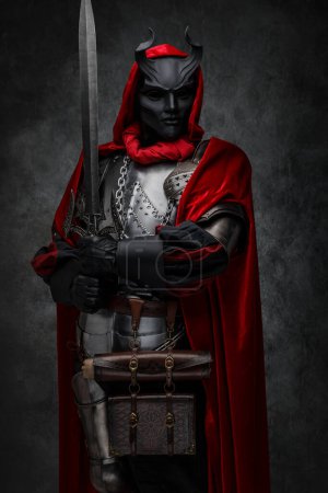 Foto de Disparo de líder de culto esotérico vestido con armadura plateada y manto rojo con máscara de cuernos. - Imagen libre de derechos