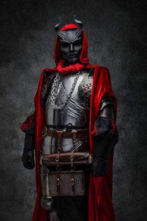 Foto de Disparo de líder de culto esotérico vestido con armadura plateada y manto rojo con máscara de cuernos. - Imagen libre de derechos