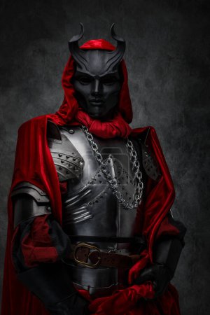 Photo for Studio shot of mystic prayer of dark cult dressed in silver plate armor and horned mask. - Royalty Free Image